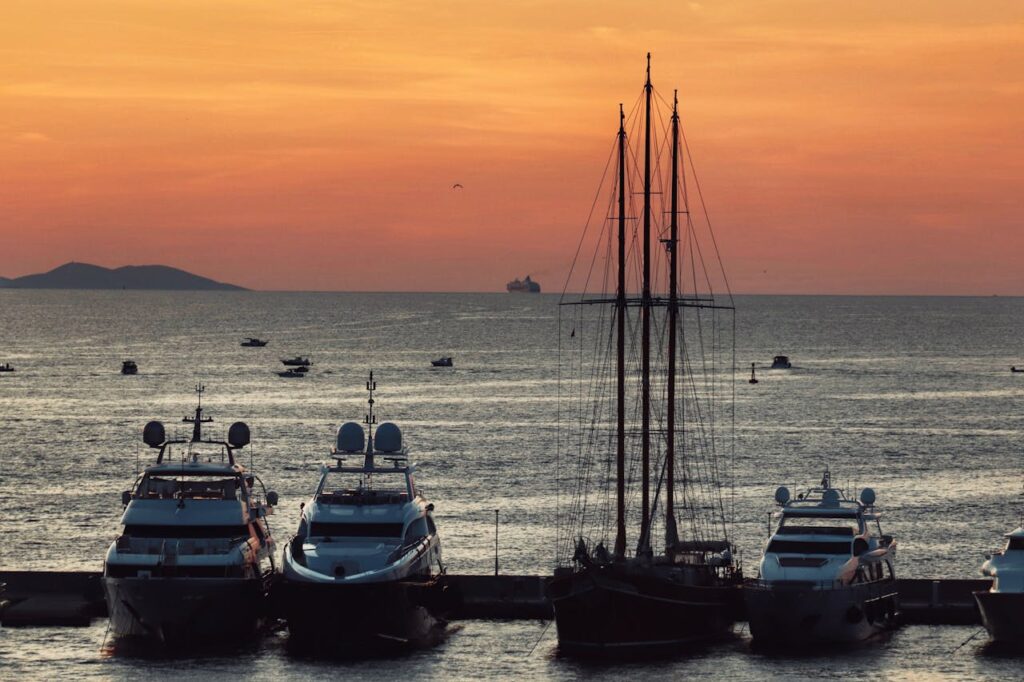 Scenic view of yachts and sailboat docked at sunset, peaceful ocean horizon.