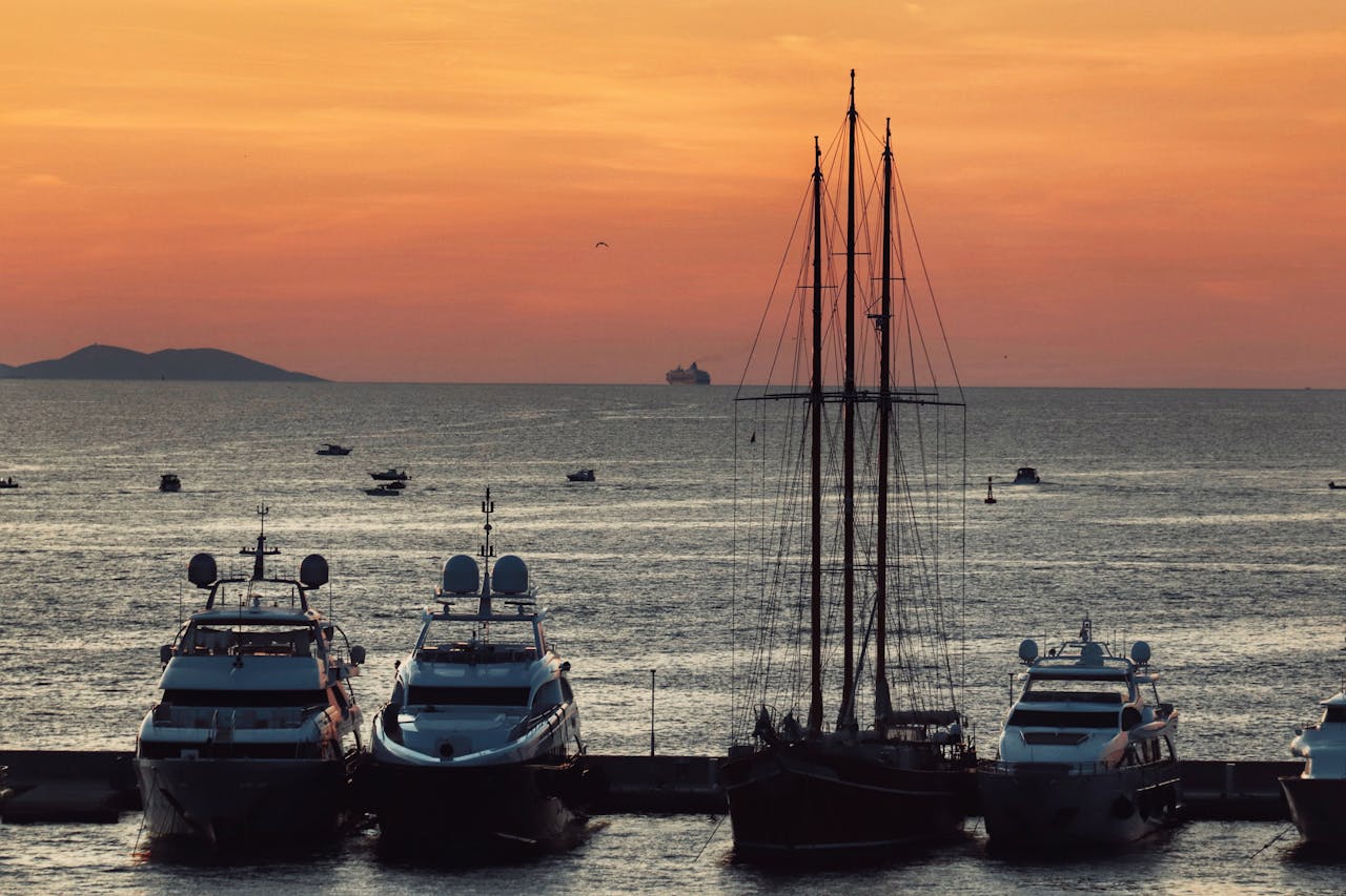 Scenic view of yachts and sailboat docked at sunset, peaceful ocean horizon.