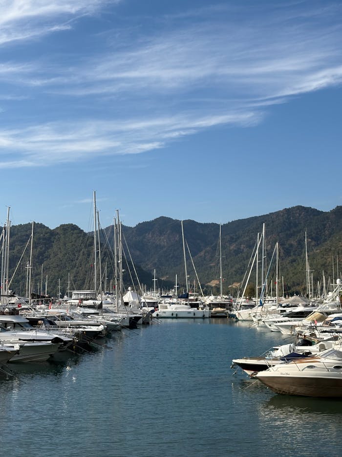 A picturesque marina with yachts against a backdrop of mountains under a clear blue sky.